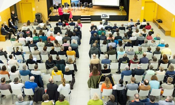 Über 200 Gäste sitzen  im Foyer der Schule auf Stühlen vor einer Bühne